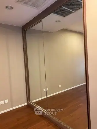 Spacious room with elegant wooden flooring and large mirrored closet doors.