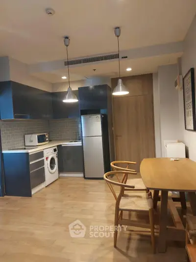 Modern kitchen with sleek cabinets, washing machine, and dining area in open layout apartment.