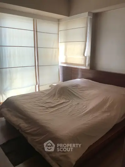 Cozy bedroom with natural light and modern wooden bed frame, perfect for relaxation.