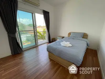 Bright and airy bedroom with hardwood flooring, a comfortable bed, and access to a sunlit balcony with a serene view, perfect for relaxation.