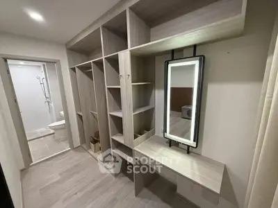 Modern walk-in closet with sleek shelving and illuminated mirror, adjacent to a stylish bathroom.