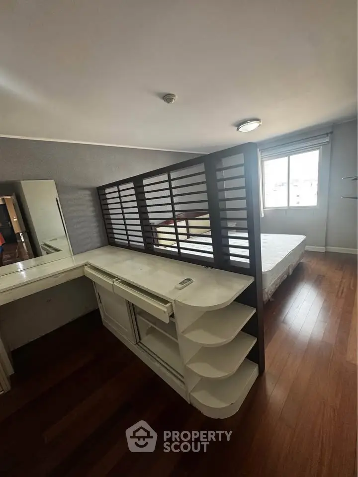 Spacious bedroom with wooden flooring and modern partition for privacy.