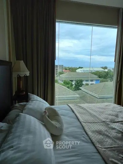 Cozy bedroom with large window offering a stunning view of the city skyline and lush greenery.