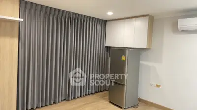Modern apartment interior with sleek fridge and elegant curtains, showcasing minimalist design and functionality.