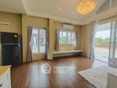Spacious living room with elegant chandelier and large windows, featuring wooden flooring and modern decor.