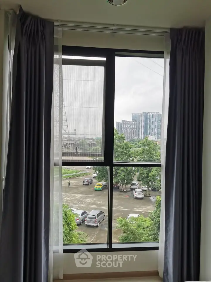 Modern apartment window with city view and parking area, offering natural light and urban living.