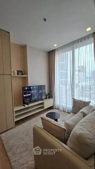 Modern living room with city view, cozy seating, and entertainment setup in a high-rise apartment.