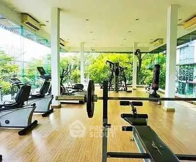 Spacious gym with modern equipment and large windows offering lush green views.