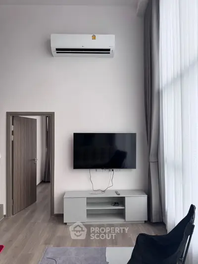 Modern living room with wall-mounted TV and air conditioning, featuring sleek furniture and floor-to-ceiling curtains.