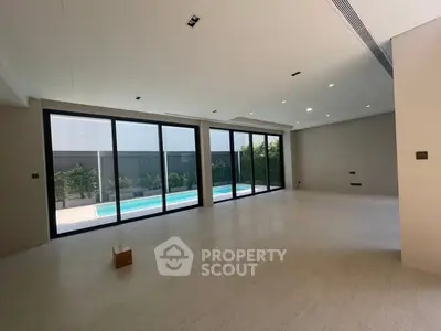 Spacious modern living room with large windows overlooking a private pool and garden.