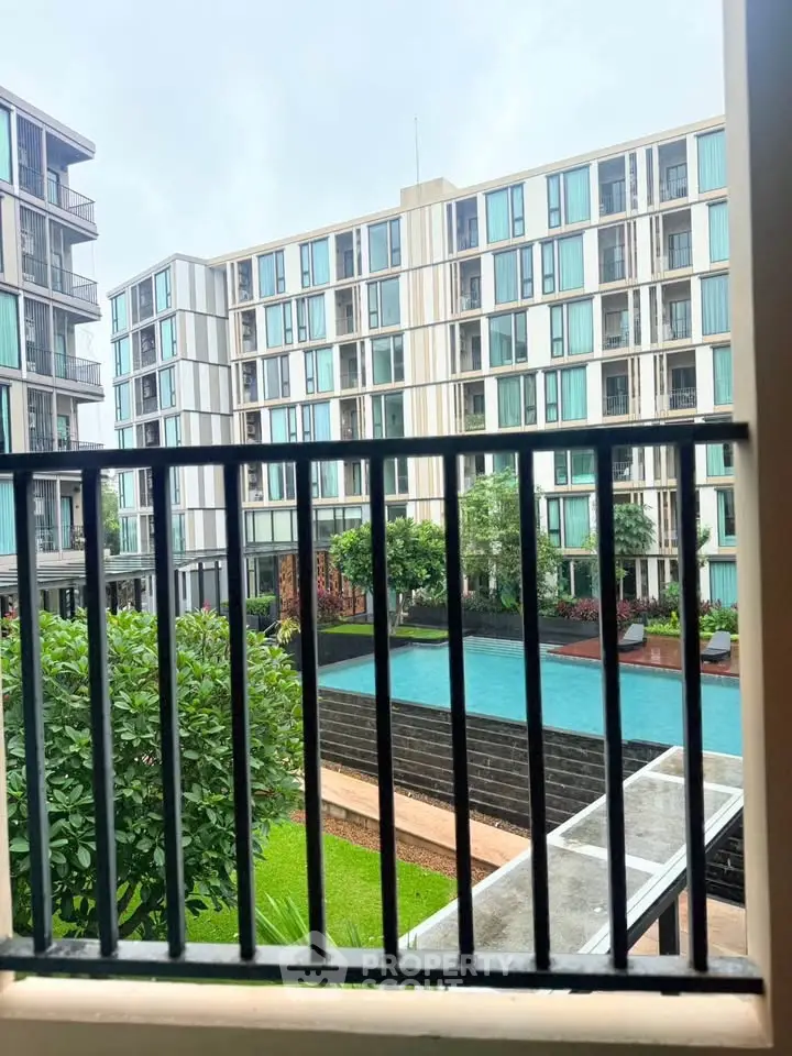 Modern apartment complex with pool view from balcony, showcasing contemporary architecture and lush greenery.