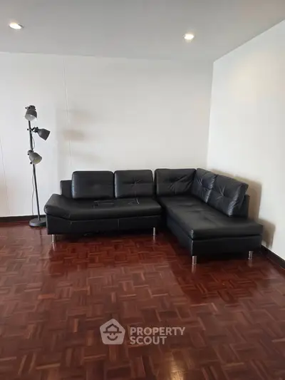 Spacious living room with sleek black leather sectional sofa and elegant parquet flooring.