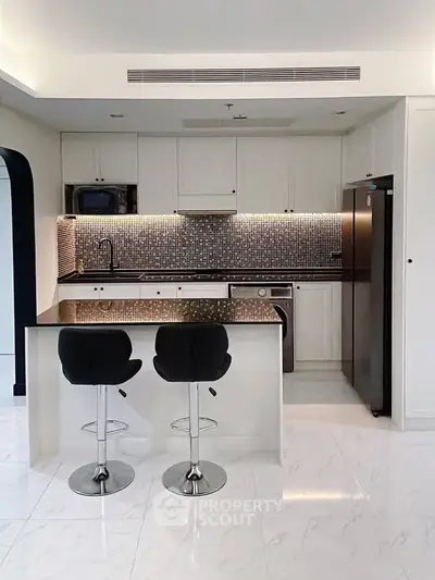 Modern kitchen with sleek design, featuring an island, bar stools, and stylish backsplash.