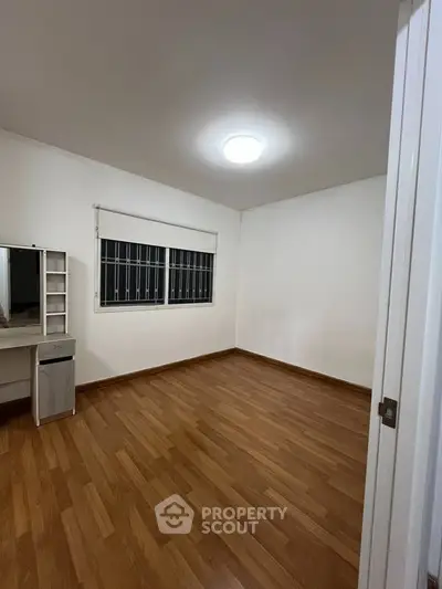 Spacious empty bedroom with wooden flooring and a large window, perfect for customization.