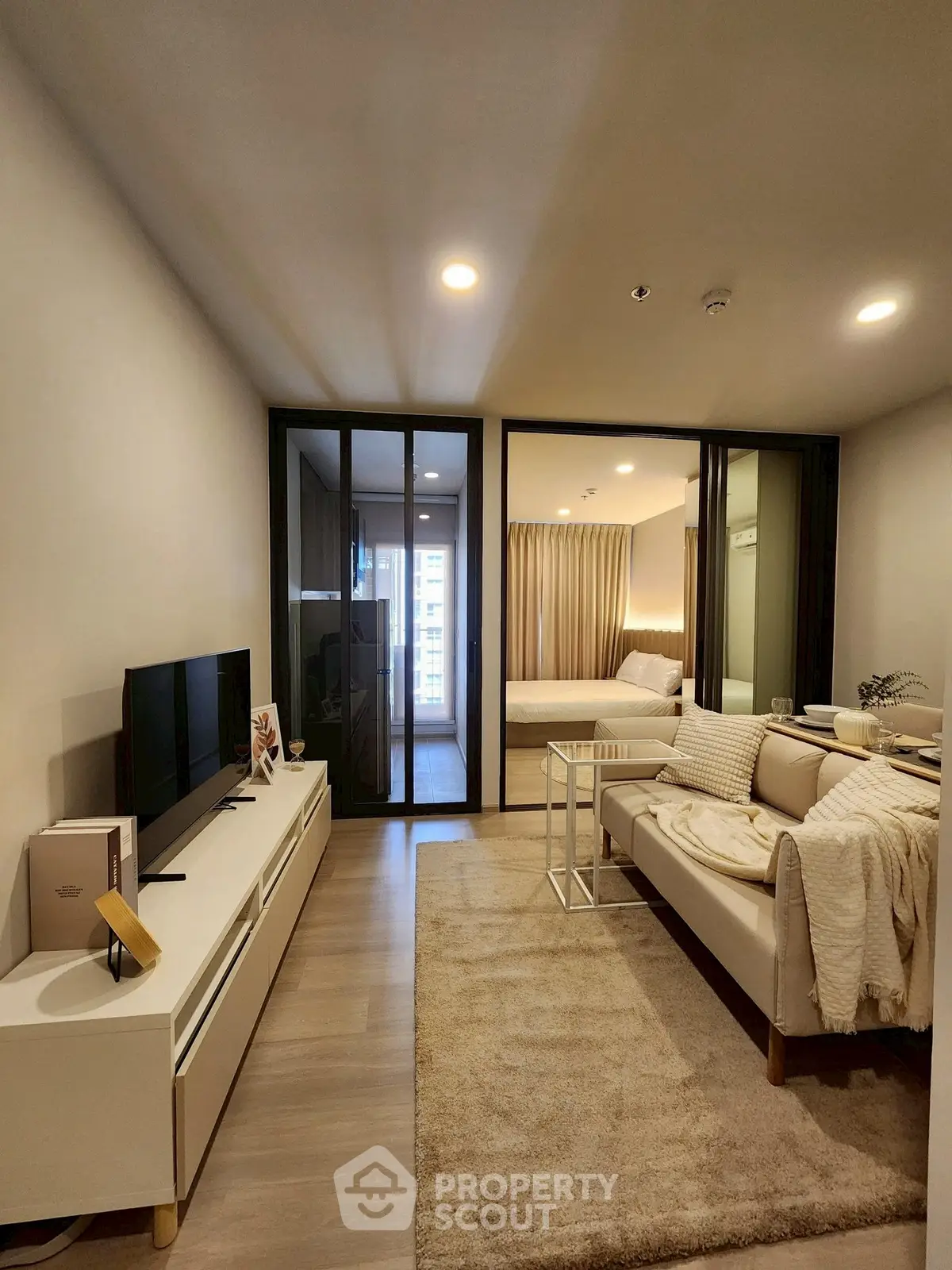 Modern living room with cozy seating and TV, leading to a stylish bedroom.