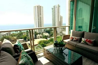 Luxurious balcony with stunning ocean view and modern outdoor seating in high-rise apartment.