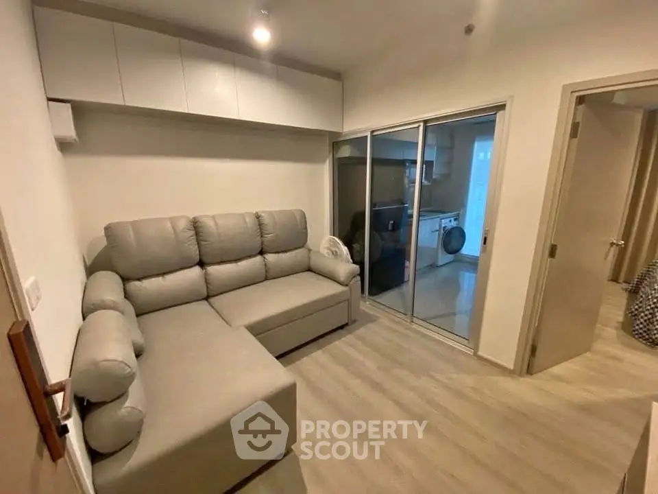 Modern living room with cozy gray sofa and sliding glass doors leading to kitchen with washing machine.