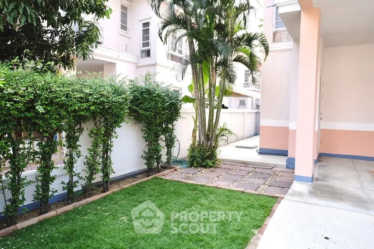 Charming garden area in a residential complex with lush greenery and paved walkway.