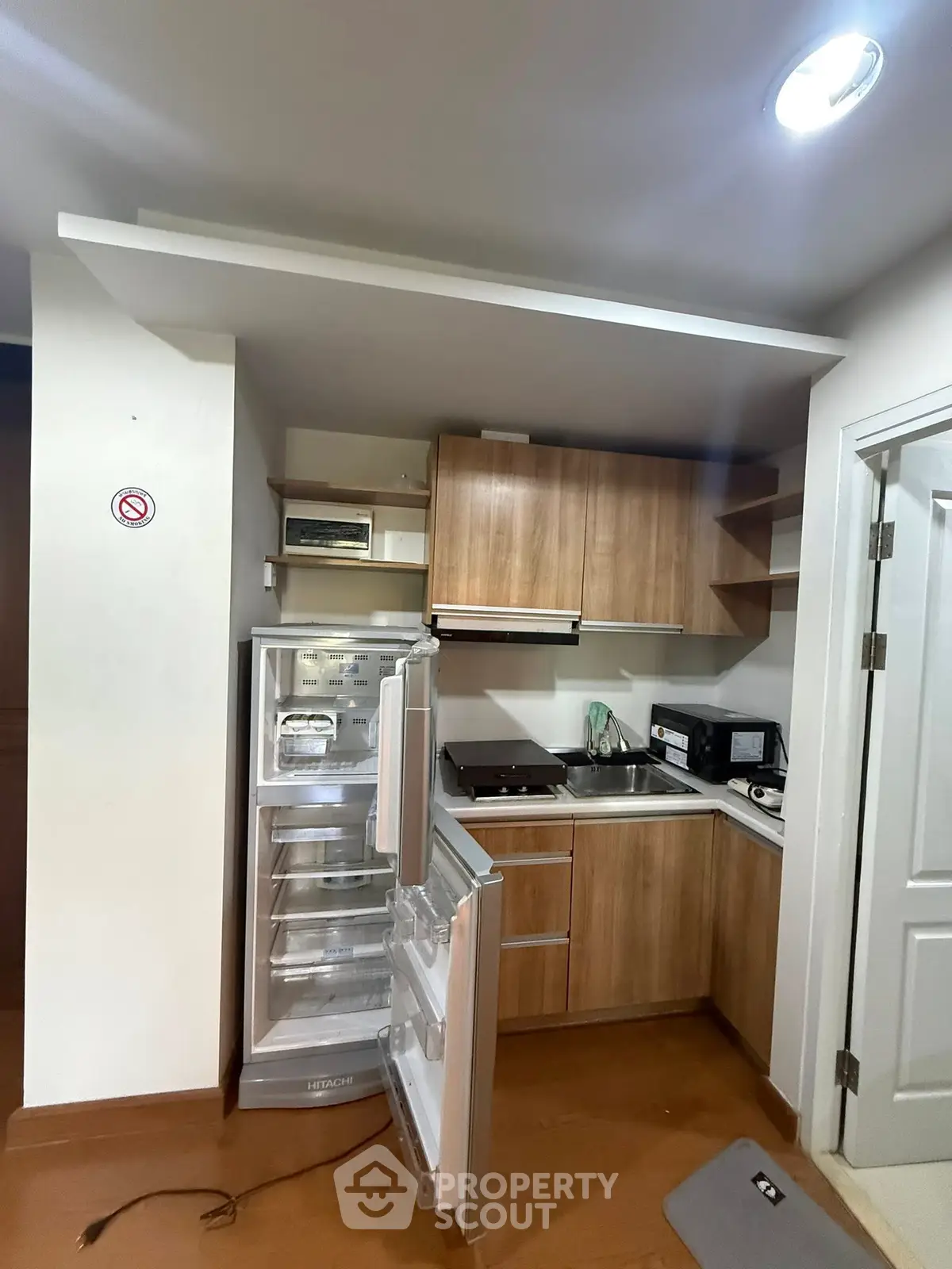 Compact kitchen with wooden cabinets, open fridge, and modern appliances in cozy apartment.