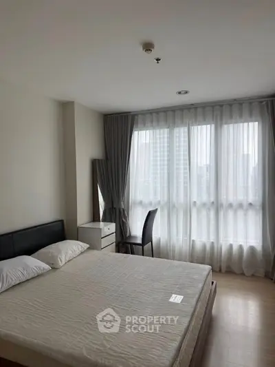 Spacious bedroom with large windows and modern furnishings in a high-rise apartment.