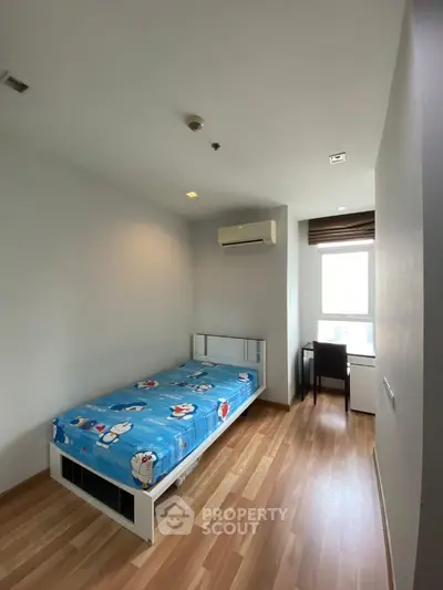 Cozy bedroom with wooden flooring and natural light, featuring a single bed and study desk.
