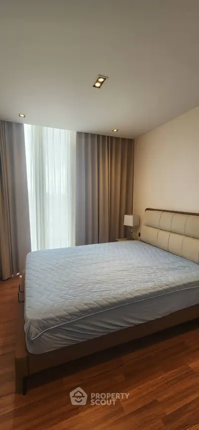 Spacious bedroom with modern decor and large window offering natural light.