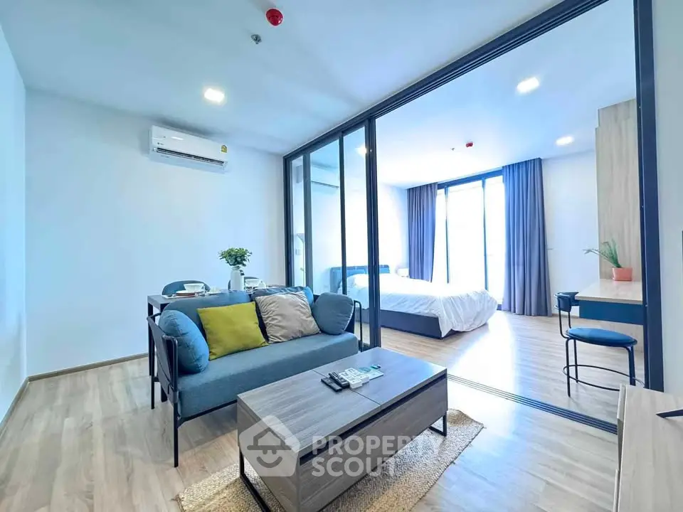 Modern open-plan living room with glass partition to bedroom, featuring stylish furniture and natural light.