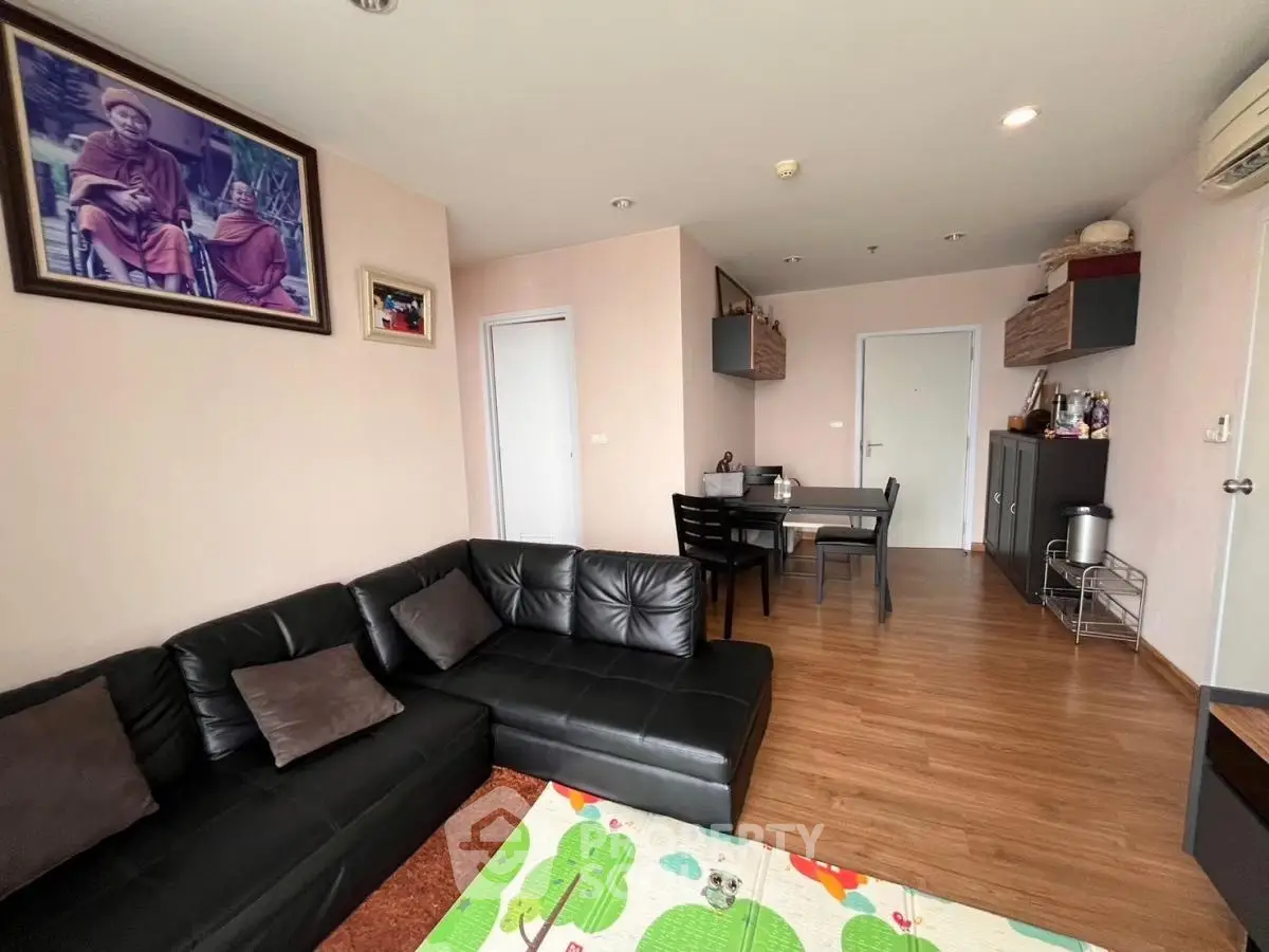 Spacious living room with modern black leather sofa and dining area in open layout apartment.