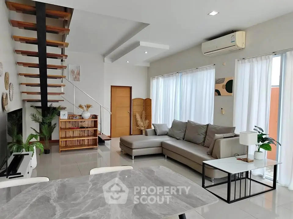Modern living room with stylish staircase, large windows, and elegant furniture in a bright, open space.