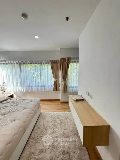 Spacious bedroom with large windows and elegant curtains, featuring a cozy bed and modern decor.