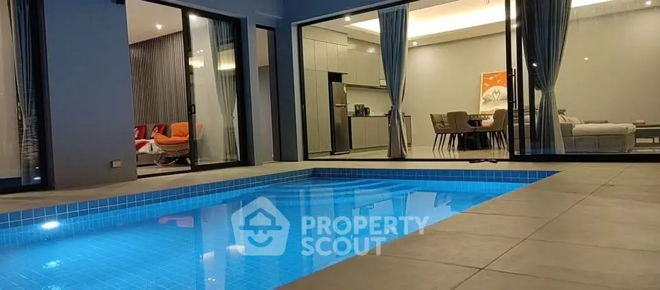 Luxurious modern home with illuminated pool and stylish open-plan living area, perfect for entertaining.