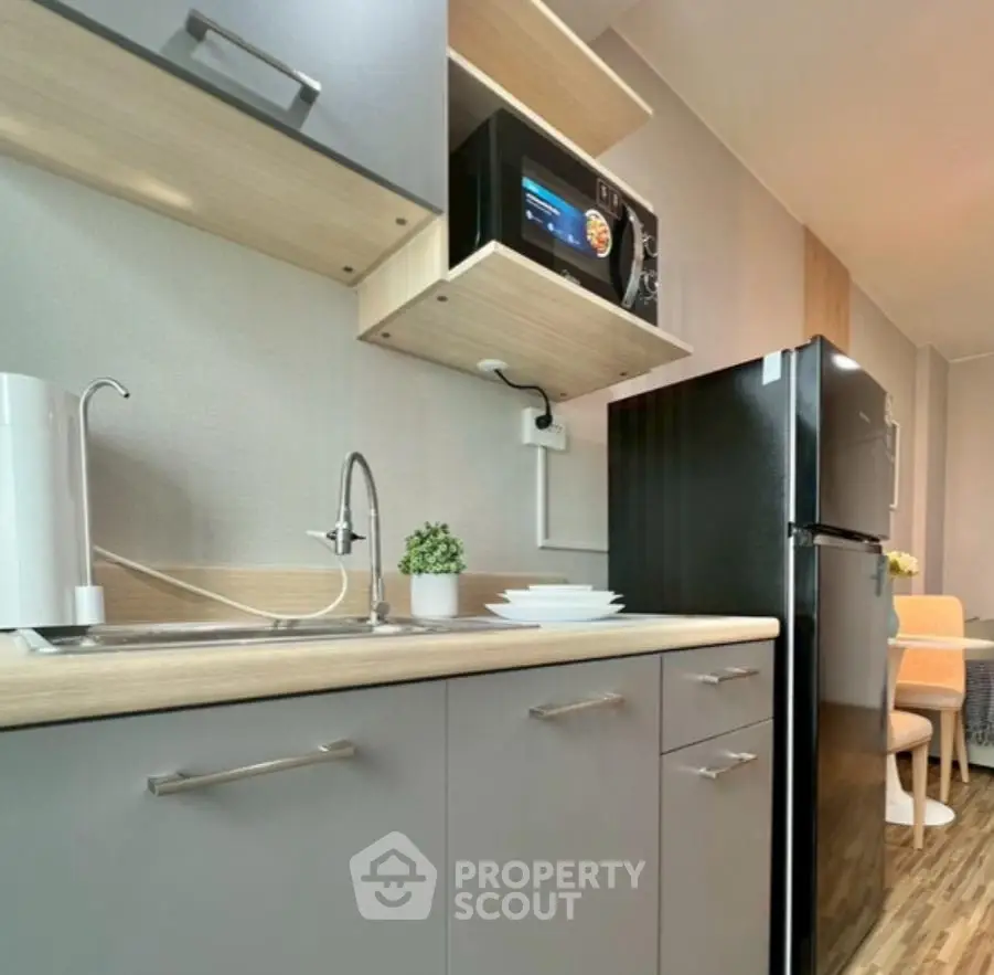 Modern kitchen with sleek cabinets, microwave, and fridge in a cozy apartment setting.