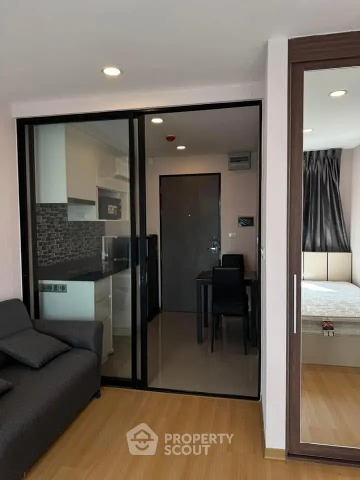 Modern apartment interior with glass partition, cozy living area, and compact kitchen.