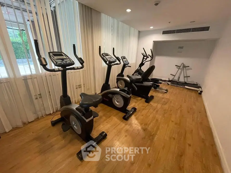 Modern gym with exercise bikes and treadmill in a well-lit space with wooden flooring.