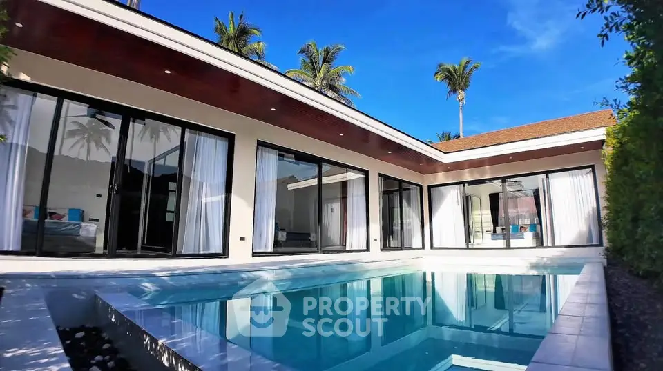 Luxurious modern villa with private pool and large glass windows under clear blue sky.