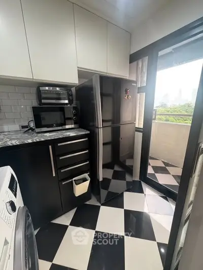 Modern kitchen with black and white checkered floor, sleek appliances, and balcony view.
