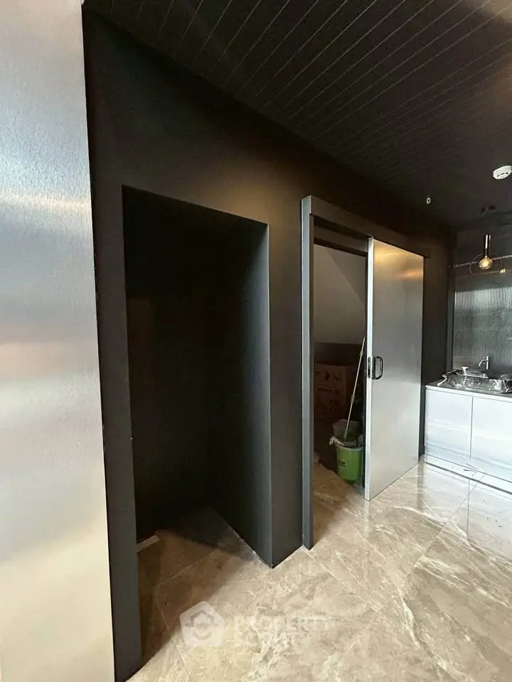 Modern kitchen with sleek black walls and sliding door, featuring stainless steel sink and marble flooring.