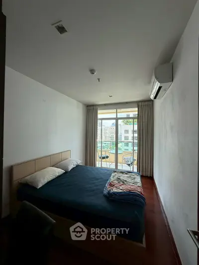 Spacious bedroom with balcony and city view, featuring a comfortable bed and air conditioning.