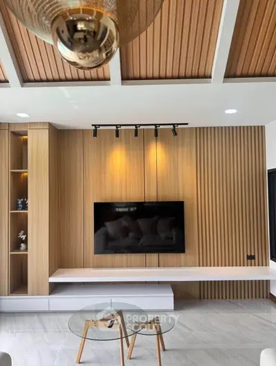Modern living room with wood paneling, sleek TV setup, and stylish glass coffee table.