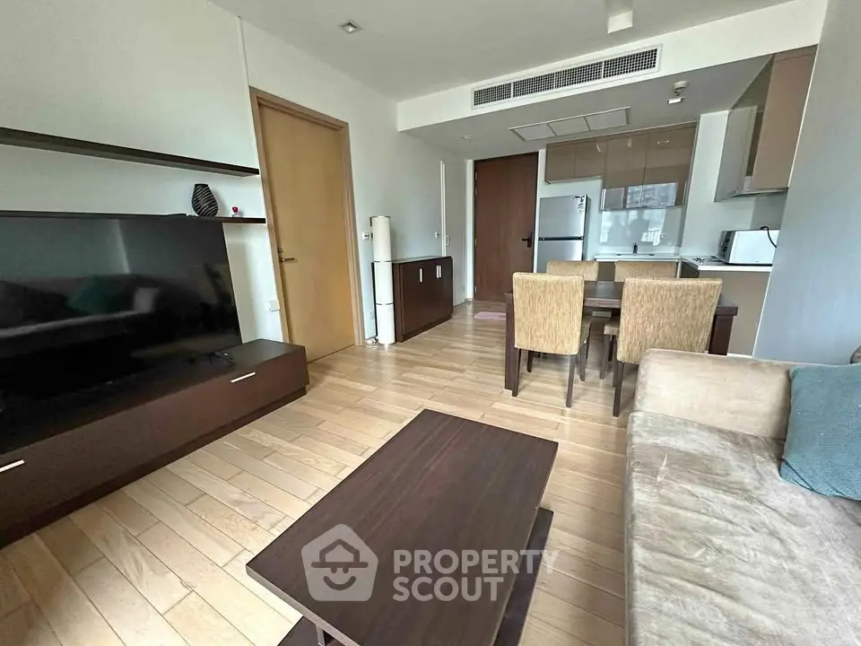 Modern living room with open kitchen, featuring sleek furniture and wooden flooring.