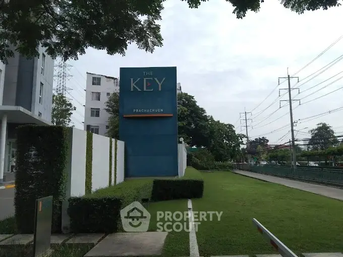 Modern residential building entrance with lush green landscaping and prominent signage.