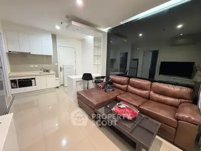 Modern living room with sleek kitchen, leather sofa, and stylish decor in open-concept apartment.