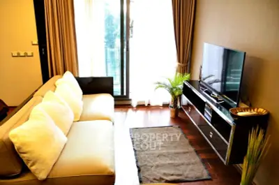 Stylish living room with cozy sofa and large TV, featuring elegant decor and natural light from balcony.