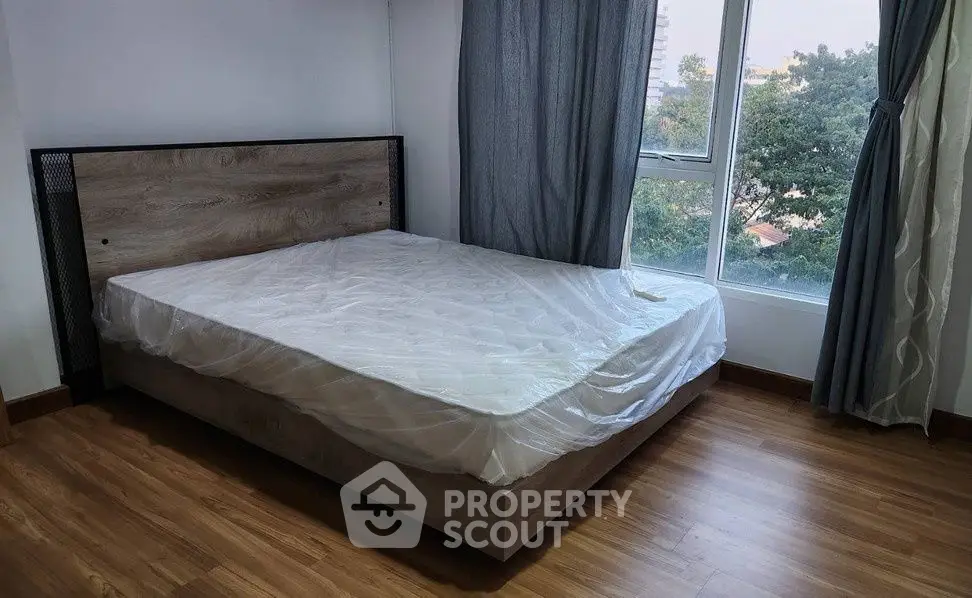 Cozy bedroom with large window and wooden flooring, offering a serene view.