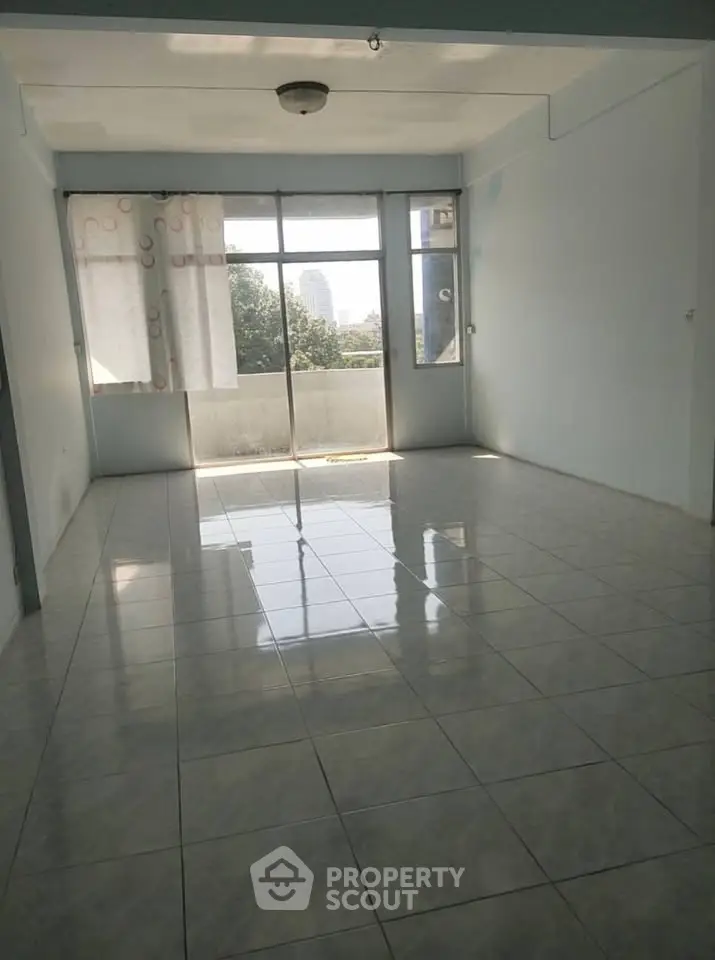 Spacious living room with large windows and tiled flooring, offering natural light and city views.