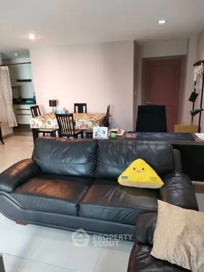 Spacious living room with modern leather sofa and dining area in open layout apartment.