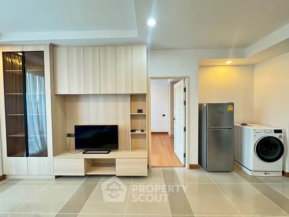 Modern living room with built-in TV unit, fridge, and washing machine in a stylish apartment.