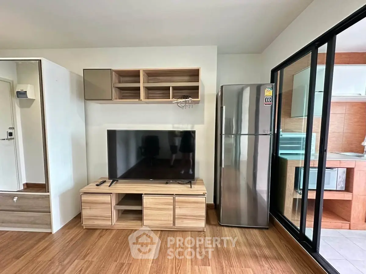 Modern living room with sleek TV unit and stainless steel fridge, featuring wooden flooring and open layout.