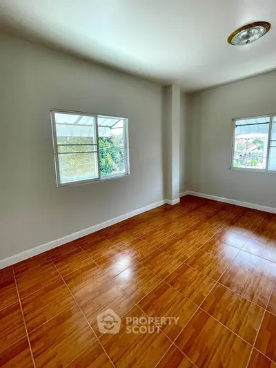 Spacious empty room with wooden flooring and large windows, perfect for customization.