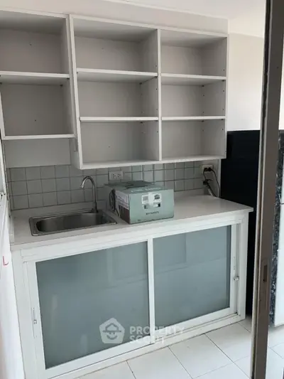 Compact kitchen with open shelving and sliding glass cabinets, featuring a single sink and tiled backsplash.